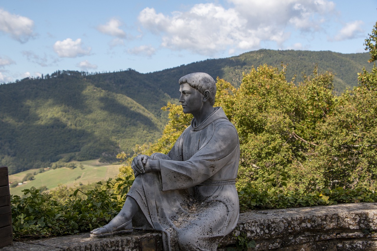 Statue of St Francis, stting on a wall, overlooking trees and fields